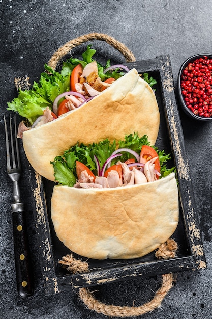 Doner kebab with grilled chicken meat and vegetables in pita bread on a wooden tray. Black background. Top view.