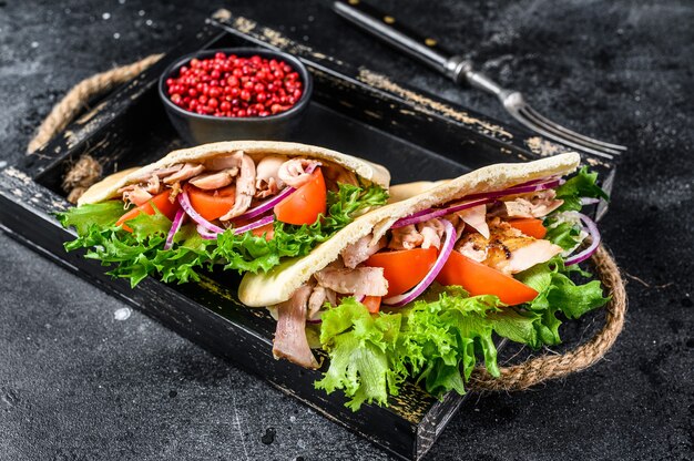 Doner kebab with grilled chicken meat and vegetables in pita bread on a wooden tray on wooden table. Top view.