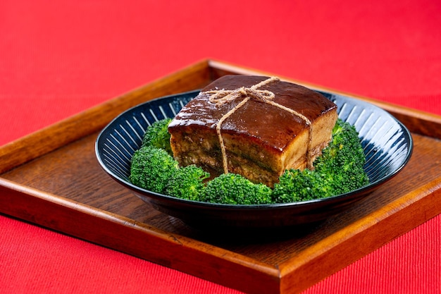 緑のブロッコリー野菜の伝統的なお祭り料理と中国の旧正月料理の食事のための美しい青いプレートの東坡肉東坡肉をクローズアップ