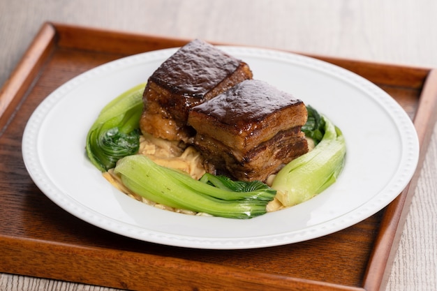 Dong Po Rou (Dongpo-varkensvlees) in een mooie blauwe plaat met groene broccoligroente, traditioneel feestelijk voedsel.