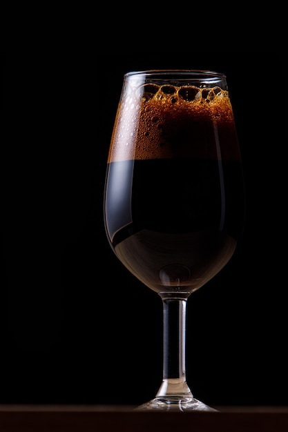 Donker bier in een glas op een donkere muur.