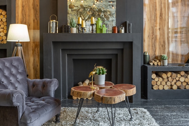 Donker brutaal interieur van zitkamer versierd met houten logboeken. gele en grijze zachte fauteuils, groot boograam en open haard