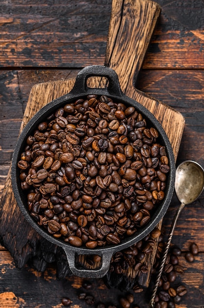 Donker gebrande koffiebonen in een pan op houten tafel. Bovenaanzicht.