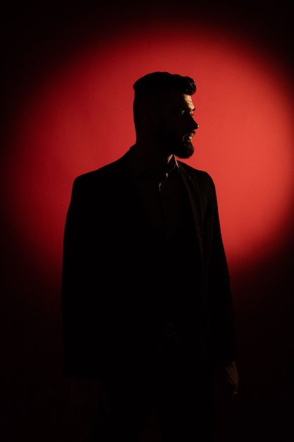 Donker mannelijk silhouet. Silhouet van de mens met baard over rode achtergrond met exemplaarruimte