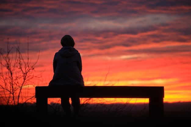 Donker silhouet van een eenzame vrouw die geniet van de zonsondergang in de avond natuur. Eenzaamheid en eenzaamheid concept.