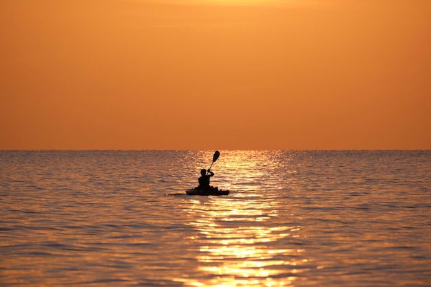 Donker silhouet van eenzame visser die op zijn boot op zeewater roeit bij zonsondergang