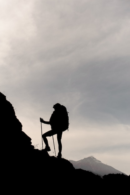 Donker silhouetmeisje dat zich op de rotsen met wandelingsrugzak en wandelstokken bevindt