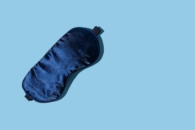 Donkerblauw slaapmasker op lichtblauwe achtergrond met kopieerruimte Minimaal concept van rust kwaliteit van slaap goede nacht slapeloosheid ontspanning Plat leggen