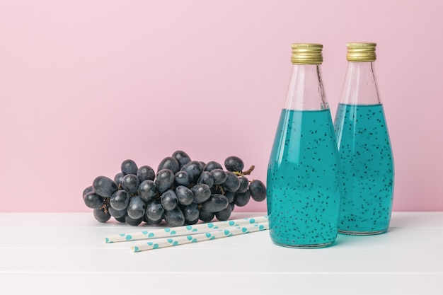 Donkerblauwe druiven en twee flessen cocktail met basilicumzaden op een roze oppervlakte