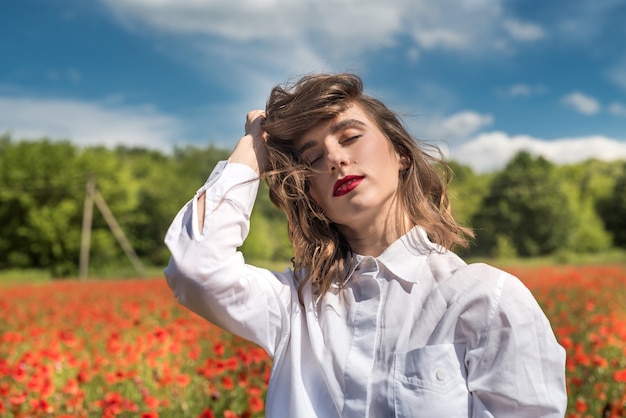 Donkerbruin meisje dat in witte blouse langs een papavergebied loopt