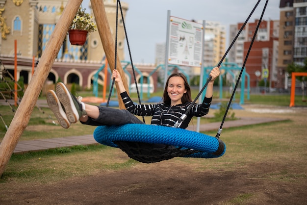 Donkerbruin meisje die op een hangende schommeling in het Park slingeren die met plezier glimlachen