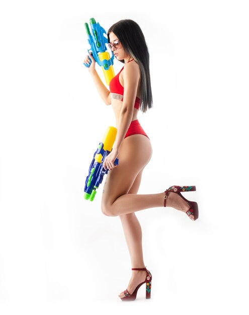 Donkerbruin meisje met een waterpistool in een rood zwempak, slank en sexy geïsoleerd op een witte achtergrond