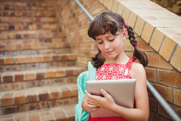 Donkerbruin schoolmeisje dat haar digitale tablet kijkt