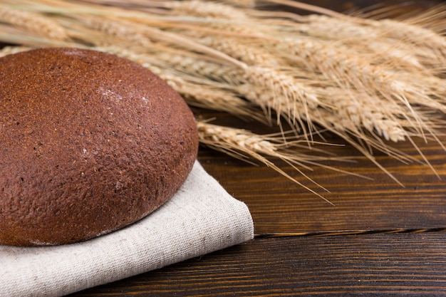 Donkerbruin volkoren of roggebrood met oren van rijpe tarwe achter op een rustieke houten tafel