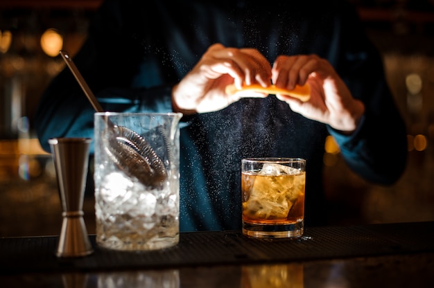 Donkerbruine barman die een jus d'orange aan de cocktail toevoegt