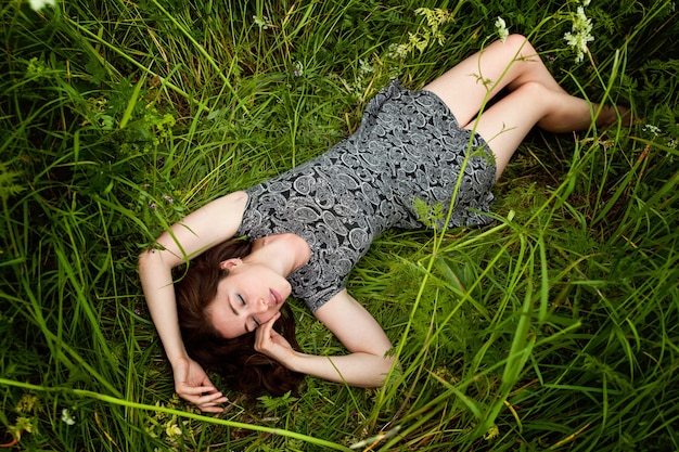 Donkerbruine jonge vrouw die op groen gras ligt. schoonheid meisje buiten genieten van natuur en ontspanning