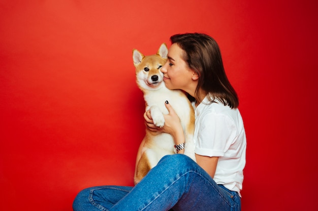 Donkerbruine vrouw die en Shiba Inu-hond, rode achtergrond omhelzen kussen