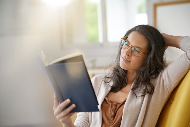 Donkerbruine vrouw die thuis boek leest