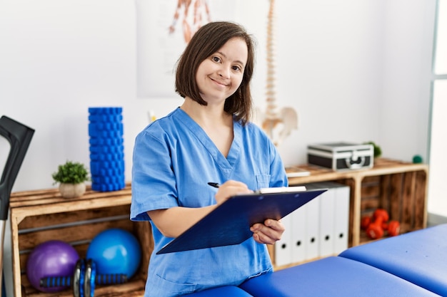 Donkerbruine vrouw met het syndroom van down die klembord houdt in de kliniek voor fysiotherapie