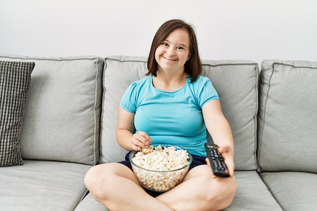 Donkerbruine vrouw met het syndroom van Down zittend op de bank tv kijkend popcorn etend in de woonkamer