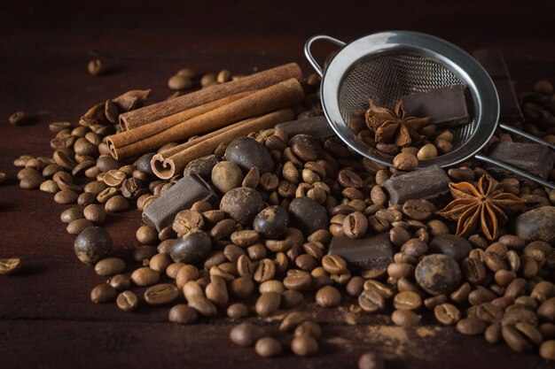 Donkere chocolade, kruiden, koffiebonen en metalen zeef op een houten oppervlak