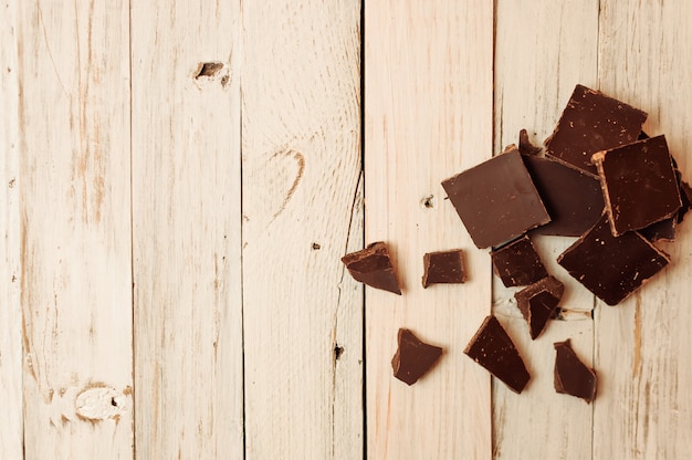 Donkere chocolade zonder suiker en glutenvrij voor diabetici en allergieën. Zwarte chocolade in stukjes gebroken ligt op een witte tafel in een rustieke stijl.