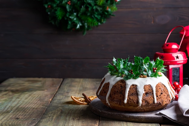 Donkere chocoladecake van Kerstmis verfraaid met witte suikerglazuur en hulstbessentakken met rode lantaarn donkere houten