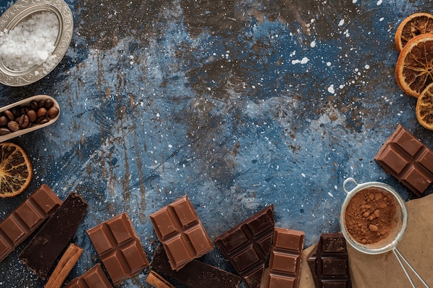 Donkere en melkchocoladerepen met droge sinaasappelplakken, kaneelstokjes en koffiebonen op blauwe ondergrond,