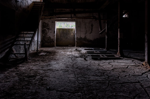 Donkere fabrieksruimte met gebarsten vuil op de vloer gebroken houten trappen en overblijfselen van machines