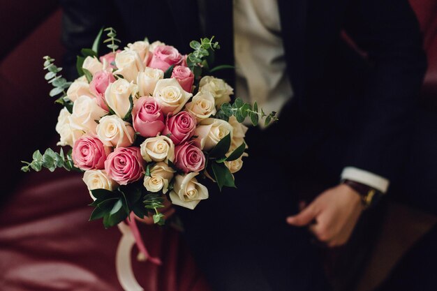 Donkere foto. Een boeket bloemen in de handen van de bruidegom op een bordeauxrode leren bank.