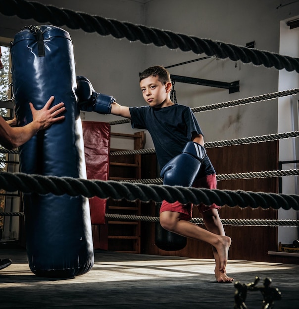 Donkere fotoshoot van kinderen die trainen met een grote bokszak in de boksstudio.