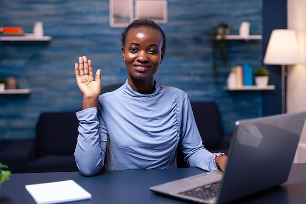 Donkere huid freelancer vrouw zwaaien naar camera in de loop van videoconferentie Zwarte freelancer werkt met team op afstand chatten virtuele online conferentie.