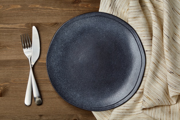 Donkere keramische plaat en verfrommeld linnen tafelkleed en bestek op een houten tafel wooden