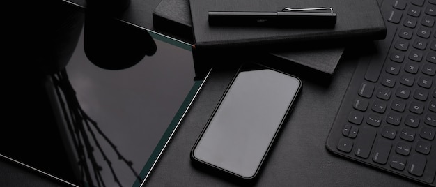 Donkere moderne werkruimte met digitale tablet, smartphone, draadloos toetsenbord, schemaboeken en pen