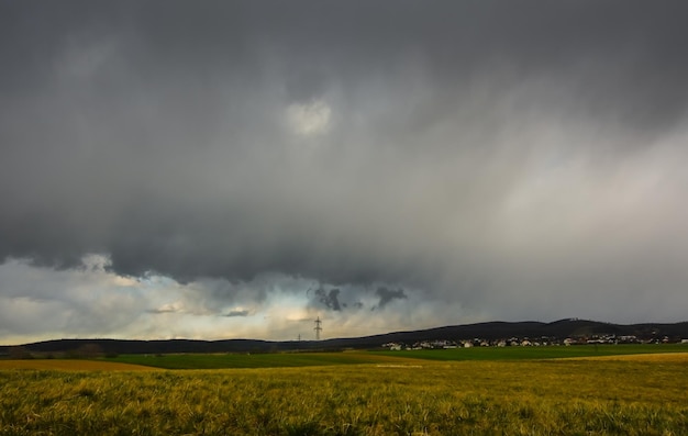 Donkere regenwolken boven een berg met huisjes en een weiland in het voorjaar