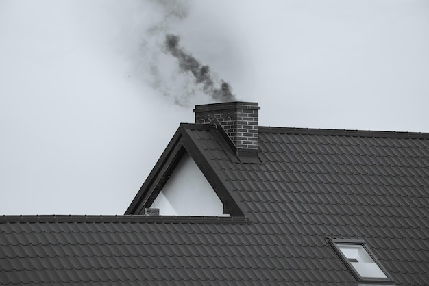 Donkere rook komt uit de schoorsteen van een modern huis in de winter Verwarming met vaste brandstof Het concept van milieuverontreiniging