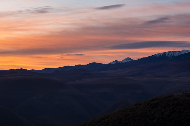Donkere silhouetten van bergen tegen een feloranje zonsonderganghemel Rode zonsondergang boven majestueuze bergen Zonsondergang in magenta tinten Sfeervol paars landschap met een besneeuwde bergvallei op grote hoogte