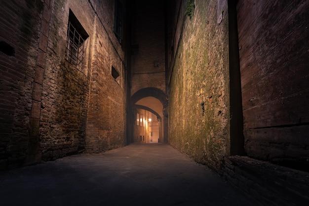 Donkere smalle lege middeleeuwse straat in het historische centrum van de Europese stad Siena, Italië