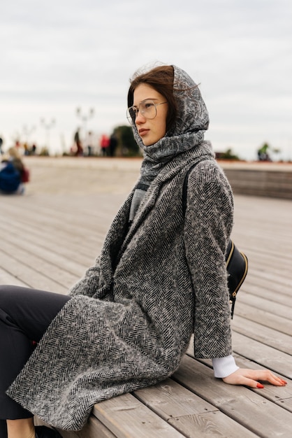 Donkerharig jong meisje met een grijze hoofddoek op haar hoofd zit buiten, draagt een bril, bewolkt weer