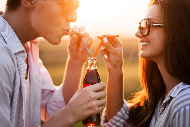 Donkerharig meisje en een jonge man drinken op een zonnige dag buiten uit een fles een drankje met rietjes. .