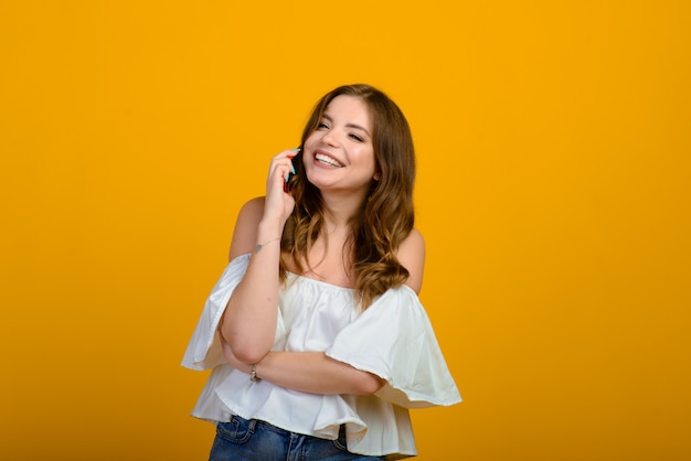 Donkerharige jonge vrouw met een glimlach en grote verraste ogen die op gele achtergrond stellen.