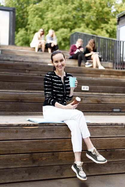 Donkerharige meisje met ijs en blauw glas koffie in haar handen zit op bankje in zomer Park, vrijetijdsconcept