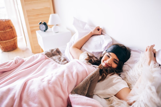 Donkerharige mooie jonge brunette wordt wakker in haar bed. Uitrekkende handen en bosdy. Liggend op bed in de slaapkamer. Alleen. 'S Ochtends genieten van de tijd.