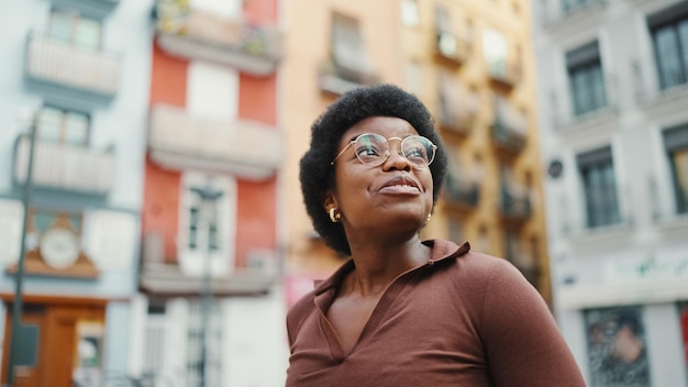 Donkerhuidig meisje met een bril die er geïnspireerd uitziet tijdens een wandeling door de stad Jonge, gelukkige Afro-vrouw die de stad verkent