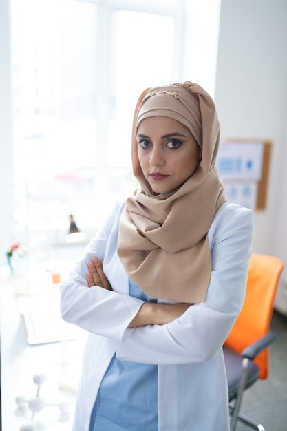 Donkerogige wetenschapper. donkerogige wetenschapper die genetica bestudeert met uniform en hijab die bij het raam staat