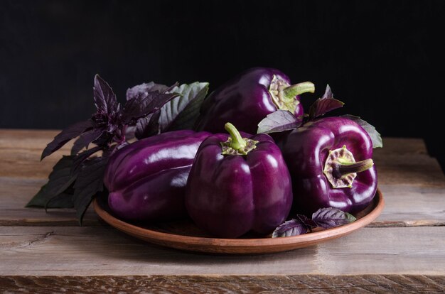 Donkerpaarse paprika's in de plaat met blaadjes basilicum