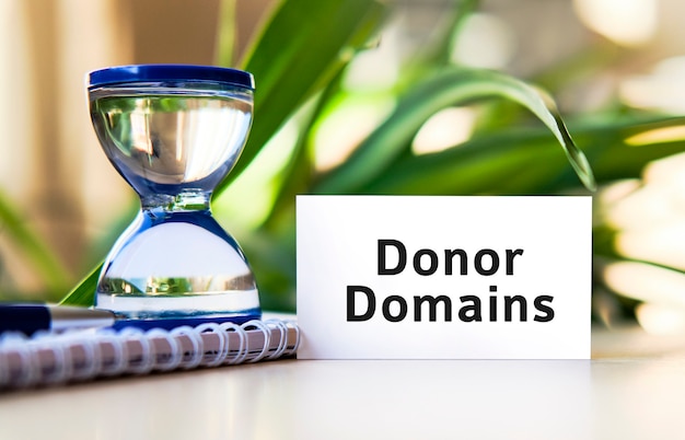 Donor domains for seo website - business concept text on a white notebook and hourglass clock, green leaves of flowers