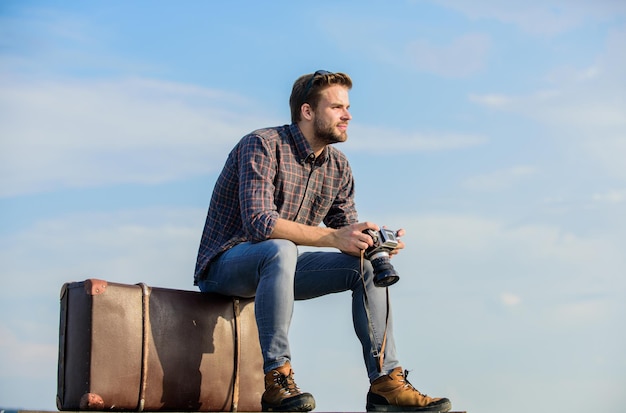 Dont forget to travel macho man tourist sit on tour bag traveler wait for flight Move sexy man sky background male fashion style looking so trendy photographer with photo camera business trip