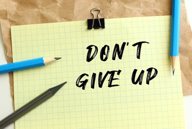 Dont give up lettering on a yellow sheet of paper over crumpled
kraft paper pencils and paper clip