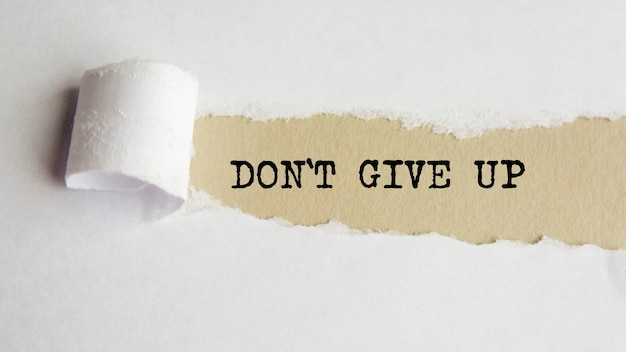DONT GIVE UP. words. text on gray paper on torn paper background.